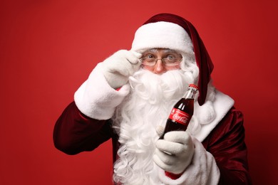 MYKOLAIV, UKRAINE - JANUARY 18, 2021: Santa Claus holding Coca-Cola bottle on red background