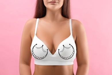 Image of Breast surgery. Woman with markings on bra against pink background, closeup