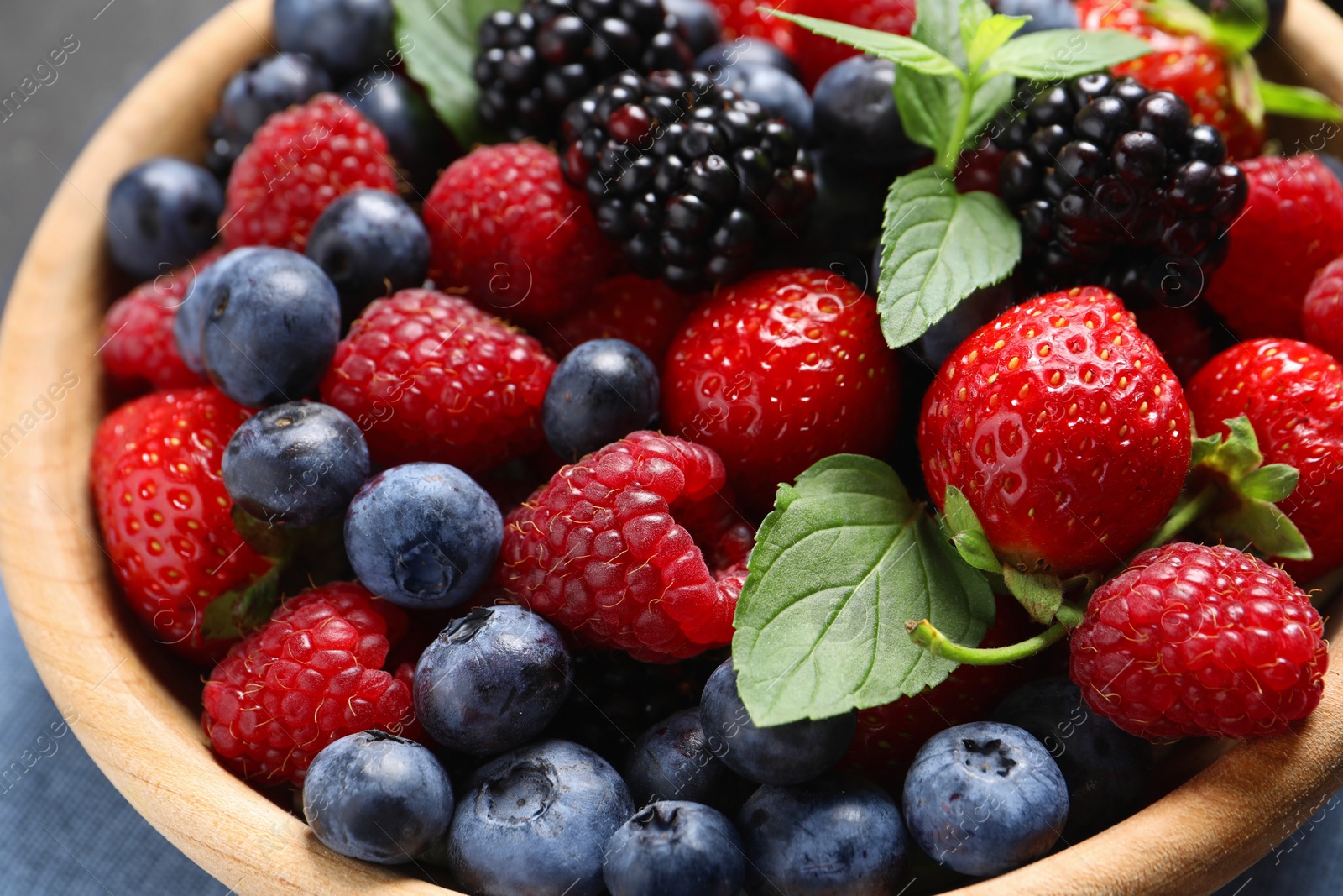 Photo of Many different fresh ripe berries in wooden bowl on black table, closeup