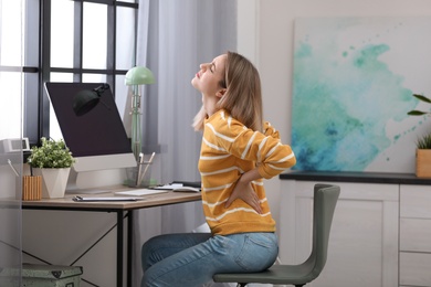 Photo of Young woman suffering from back pain in office