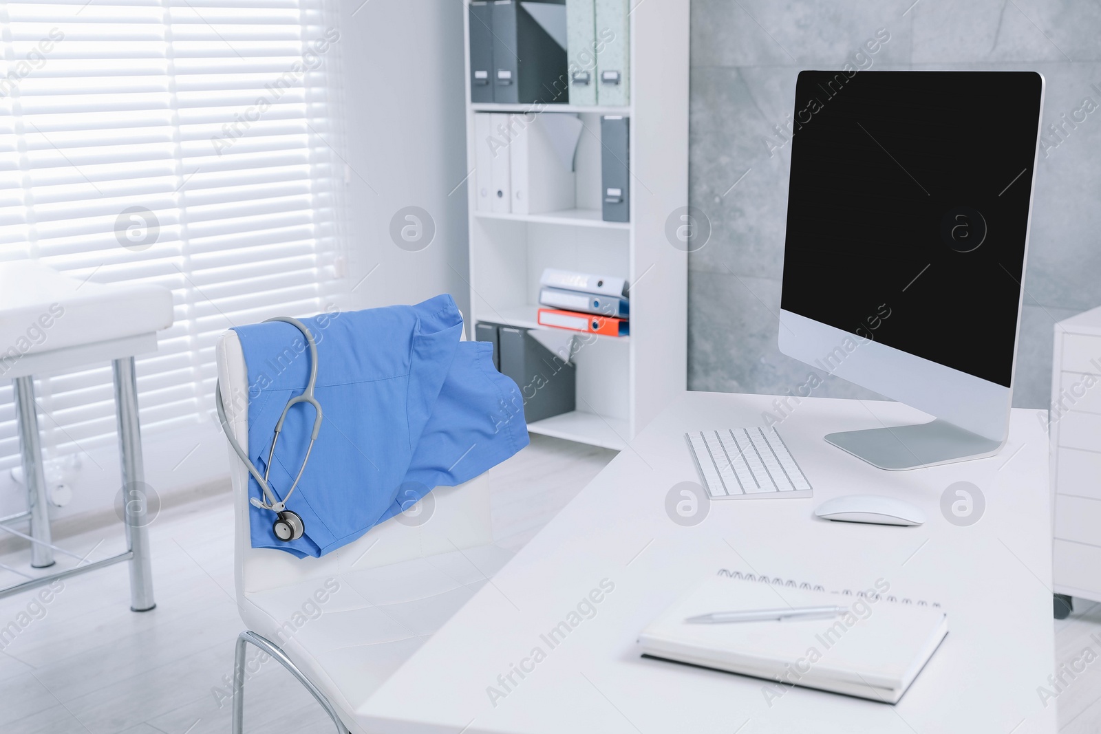 Photo of Blue medical uniform and stethoscope hanging on chair in clinic