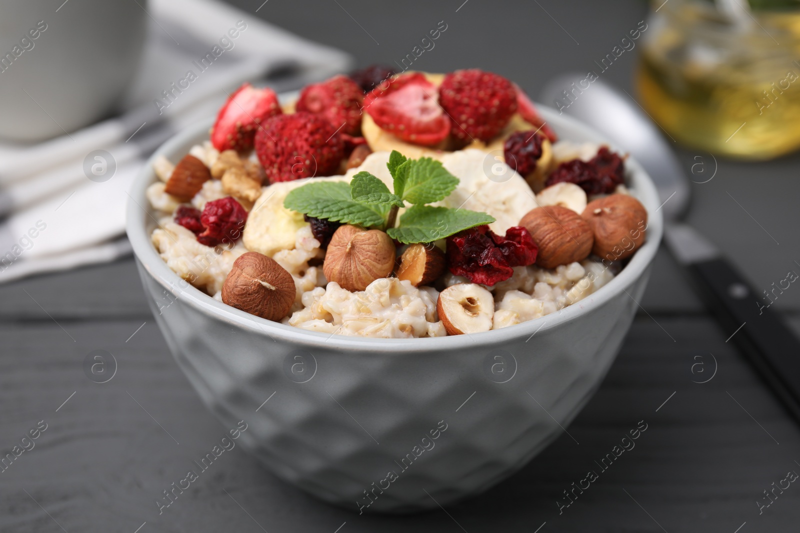 Photo of Oatmeal with freeze dried fruits, nuts and mint on grey wooden table, closeup