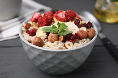 Photo of Oatmeal with freeze dried fruits, nuts and mint on grey wooden table, closeup