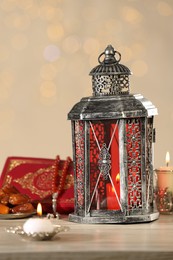 Arabic lantern, Quran, misbaha and candles on wooden table against blurred lights