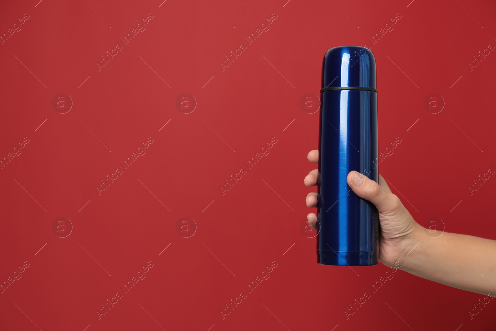 Photo of Woman holding modern blue thermos on red background, closeup. Space for text