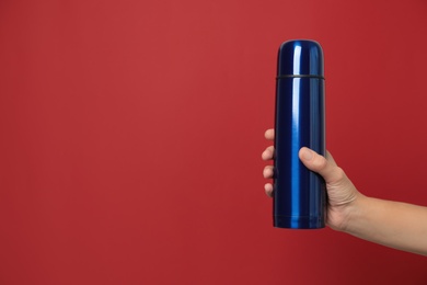 Woman holding modern blue thermos on red background, closeup. Space for text