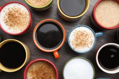 Photo of Many different cups with aromatic hot coffee on wooden table, flat lay