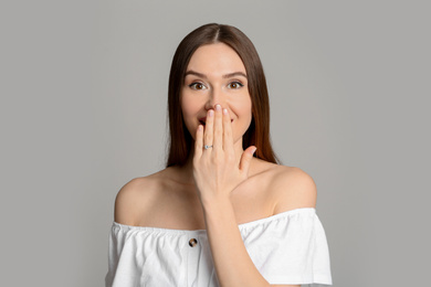 Photo of Emotional young woman wearing beautiful engagement ring on grey background