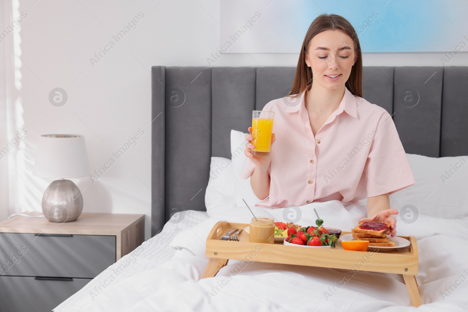 Photo of Smiling woman having breakfast in bed at home. Space for text