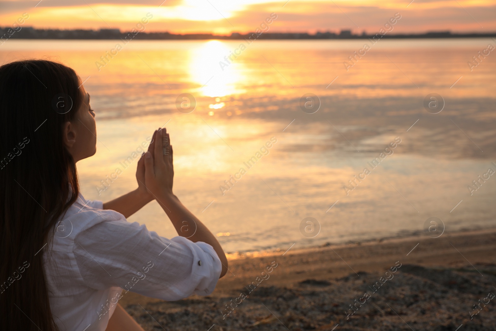 Photo of Young woman meditating near river at sunset, space for text. Nature healing power