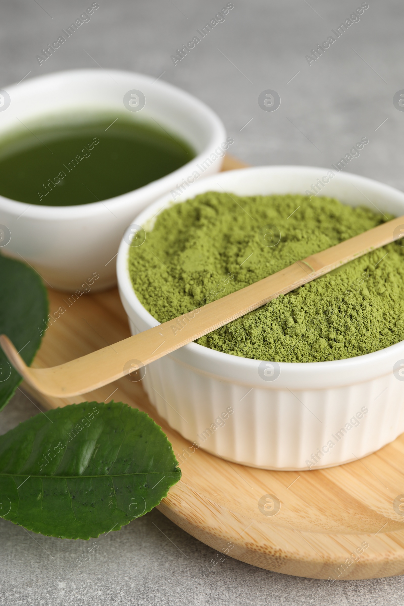 Photo of Green matcha powder and bamboo scoop on light grey table, closeup