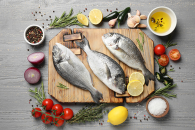 Flat lay composition with raw dorada fish on light grey wooden table