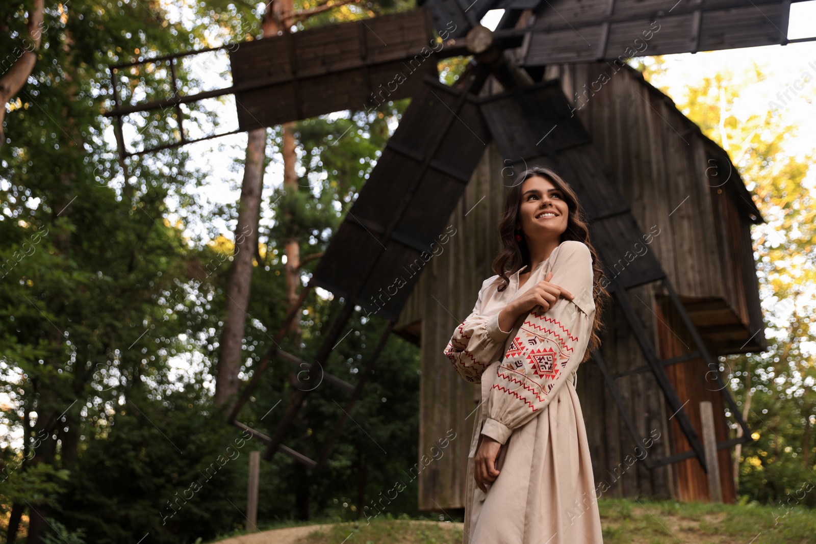 Photo of Beautiful woman wearing embroidered dress near old wooden mill in countryside. Ukrainian national clothes