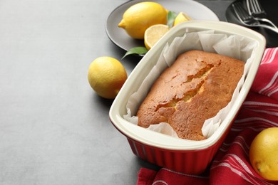 Photo of Tasty lemon cake in baking dish and citrus fruits on grey table, closeup. Space for text