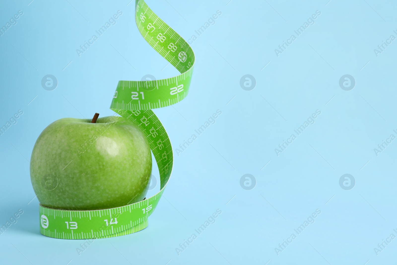 Photo of Ripe green apple and measuring tape on light blue background. Space for text