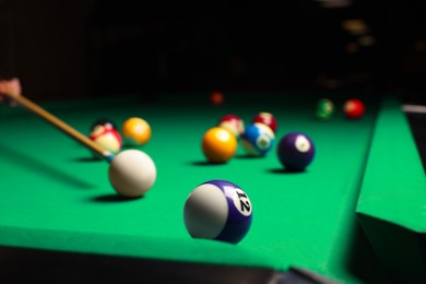 Many colorful billiard balls and cue on green table, closeup. Space for text