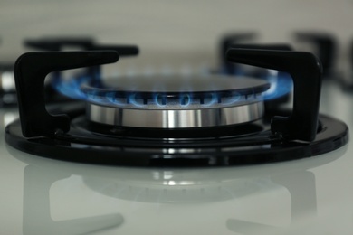 Photo of Gas burner with blue flame on modern stove, closeup