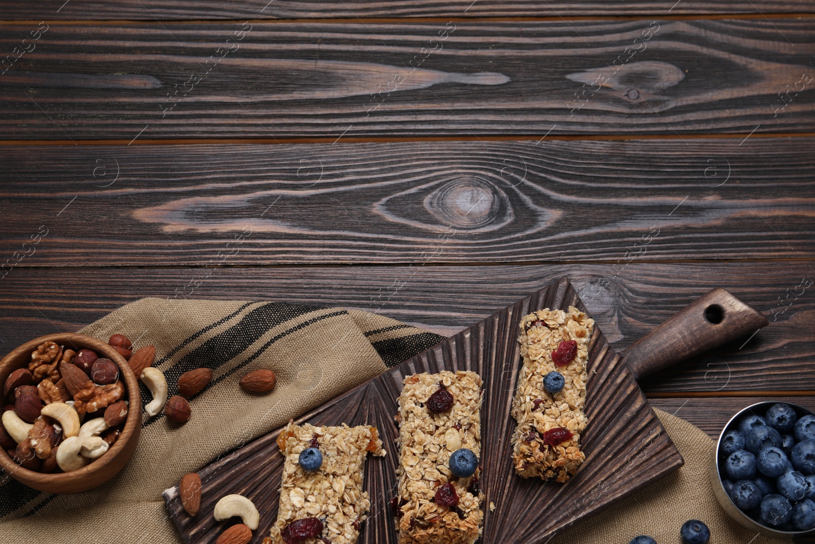 Photo of Tasty granola bars and ingredients on wooden table, flat lay. Space for text