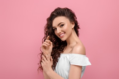 Beautiful young woman with long curly brown hair on pink background