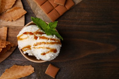 Scoops of tasty ice cream with caramel sauce, mint and candies on wooden table, flat lay. Space for text