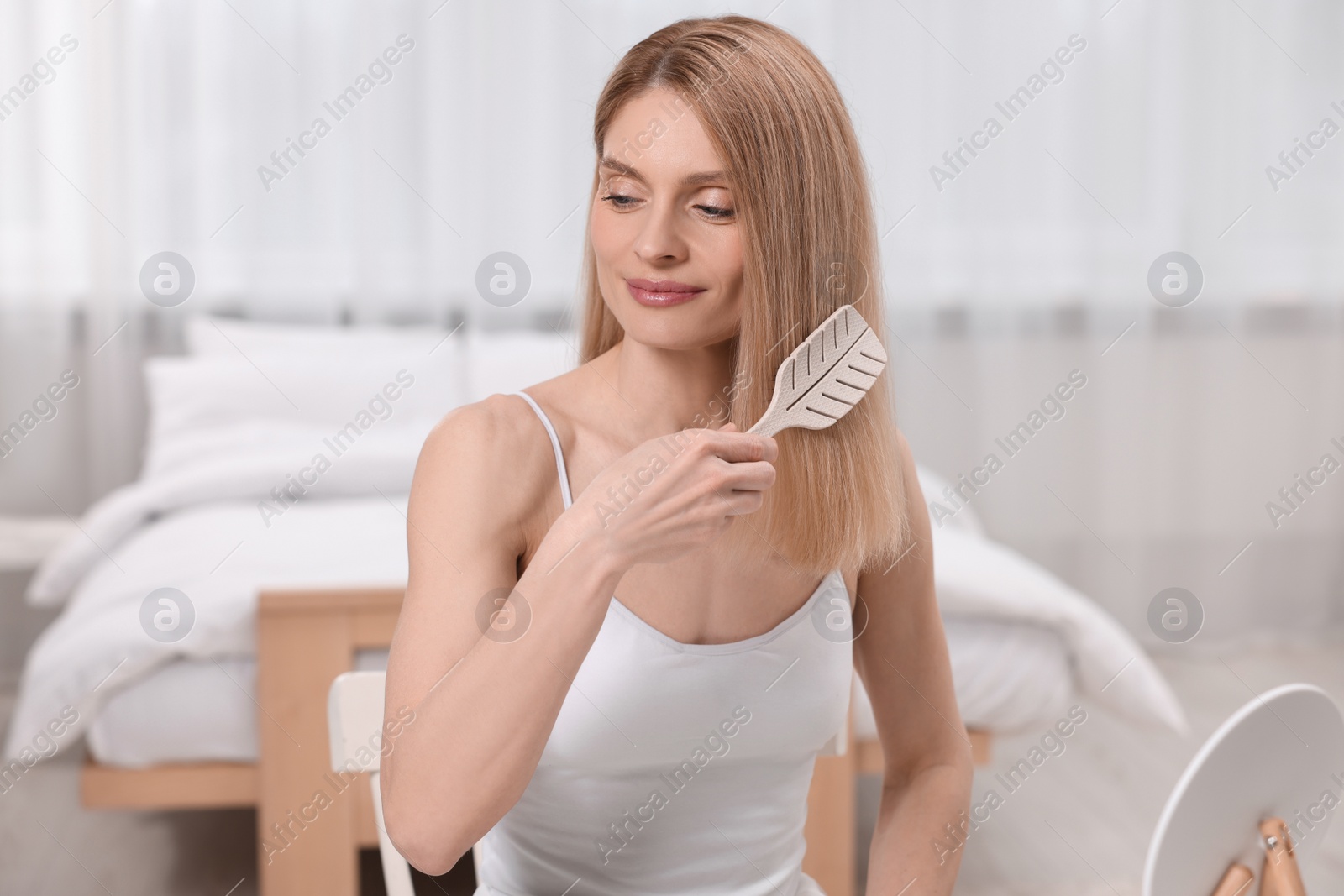 Photo of Beautiful woman brushing her hair in bedroom