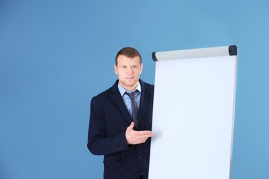 Photo of Business trainer giving presentation on flip chart board against color background