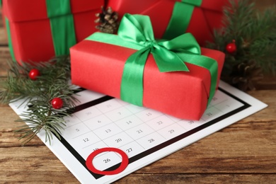 Photo of Calendar with marked Boxing Day date and gifts on wooden background, closeup