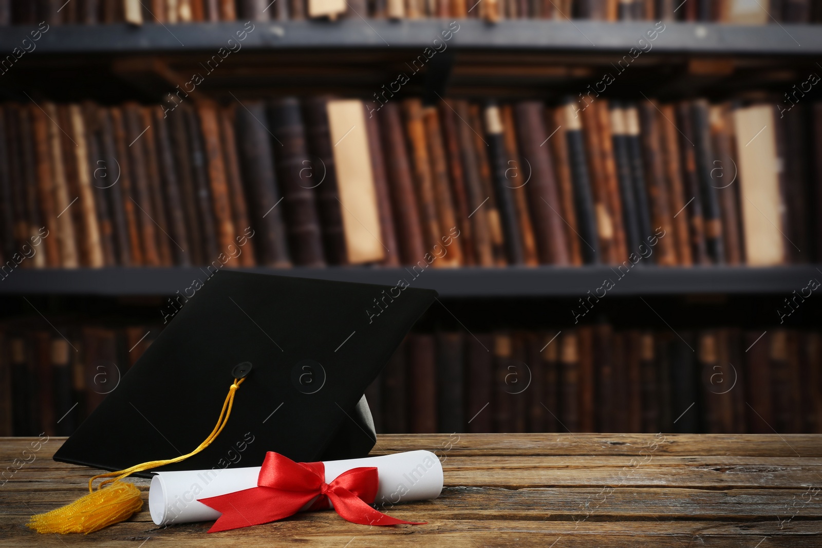 Image of Graduation hat and diploma on wooden table in library, space for text