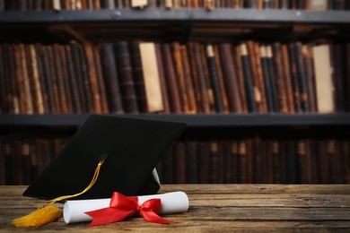 Image of Graduation hat and diploma on wooden table in library, space for text