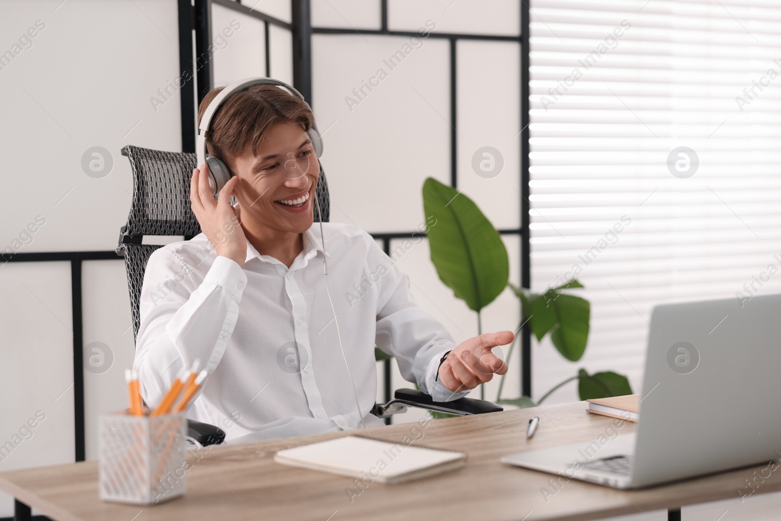 Photo of Man in headphones using video chat during webinar at wooden table in office