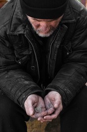 Poor homeless senior man holding coins outdoors