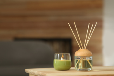 Aromatic reed air freshener and scented candle on table indoors. Space for text