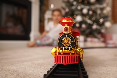 Photo of Little girl playing with colorful toy in room decorated for Christmas, focus on train