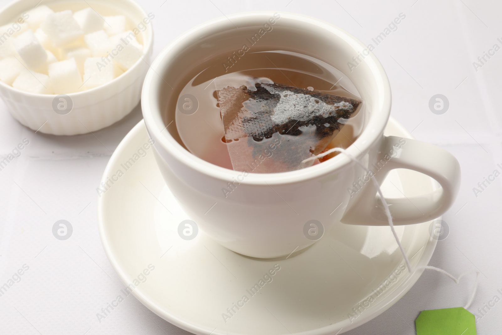 Photo of Tea bag in cup with hot drink on white table, closeup