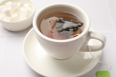 Tea bag in cup with hot drink on white table, closeup