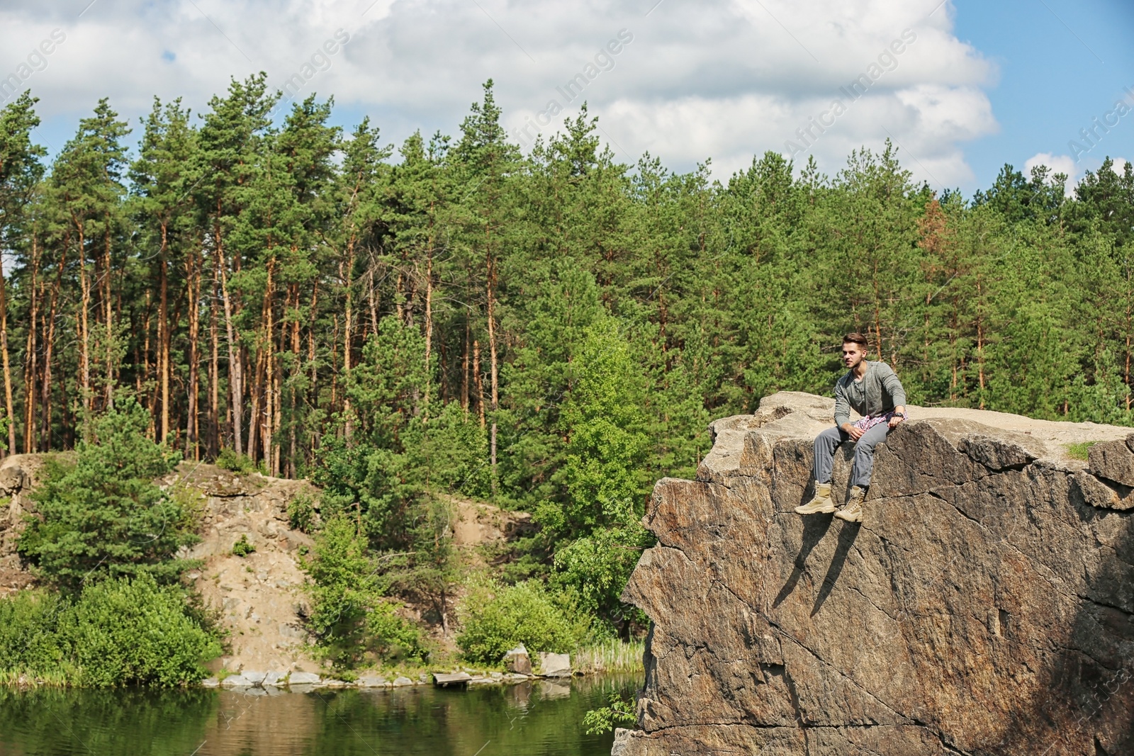 Photo of Young man on rock near lake and forest. Camping season