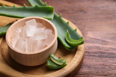 Photo of Aloe vera gel and slices of plant on wooden table, closeup. Space for text