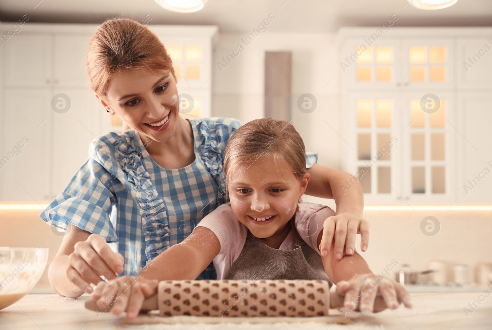 Photo of Mother and daughter rolling dough together in kitchen