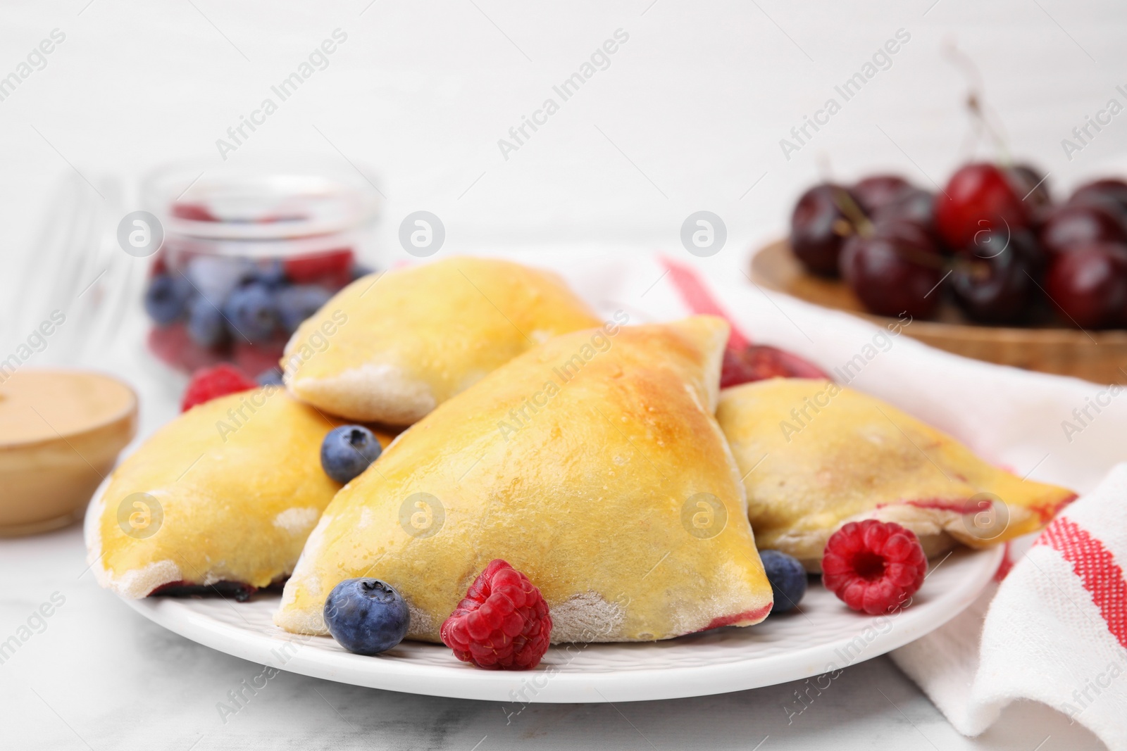 Photo of Delicious samosas with berries on white marble table, closeup