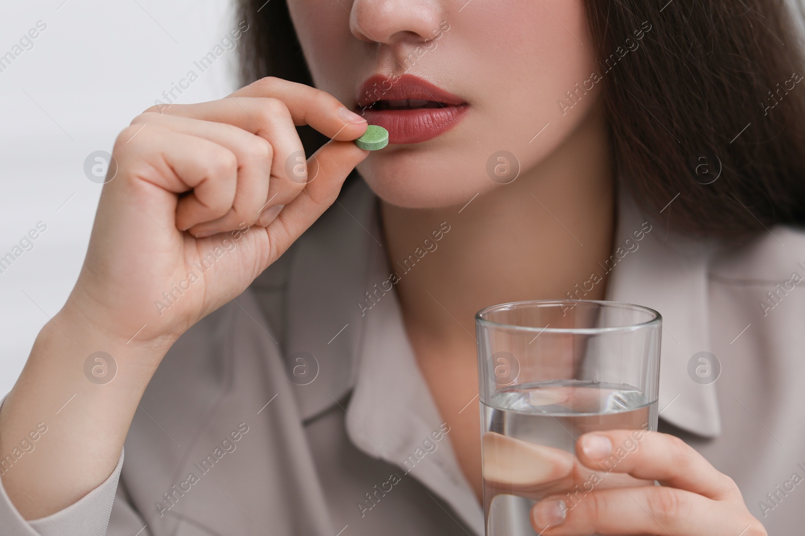 Photo of Woman with glass of water taking antidepressant pill on light grey background, closeup