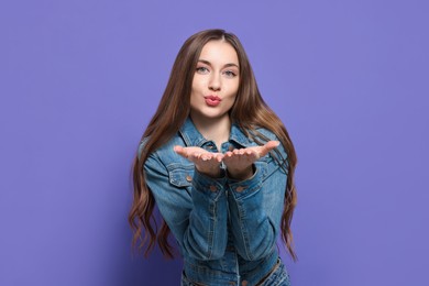 Beautiful young woman blowing kiss on purple background