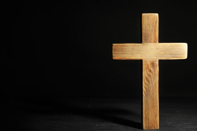 Wooden Christian cross on black slate table against dark background, space for text. Religion concept