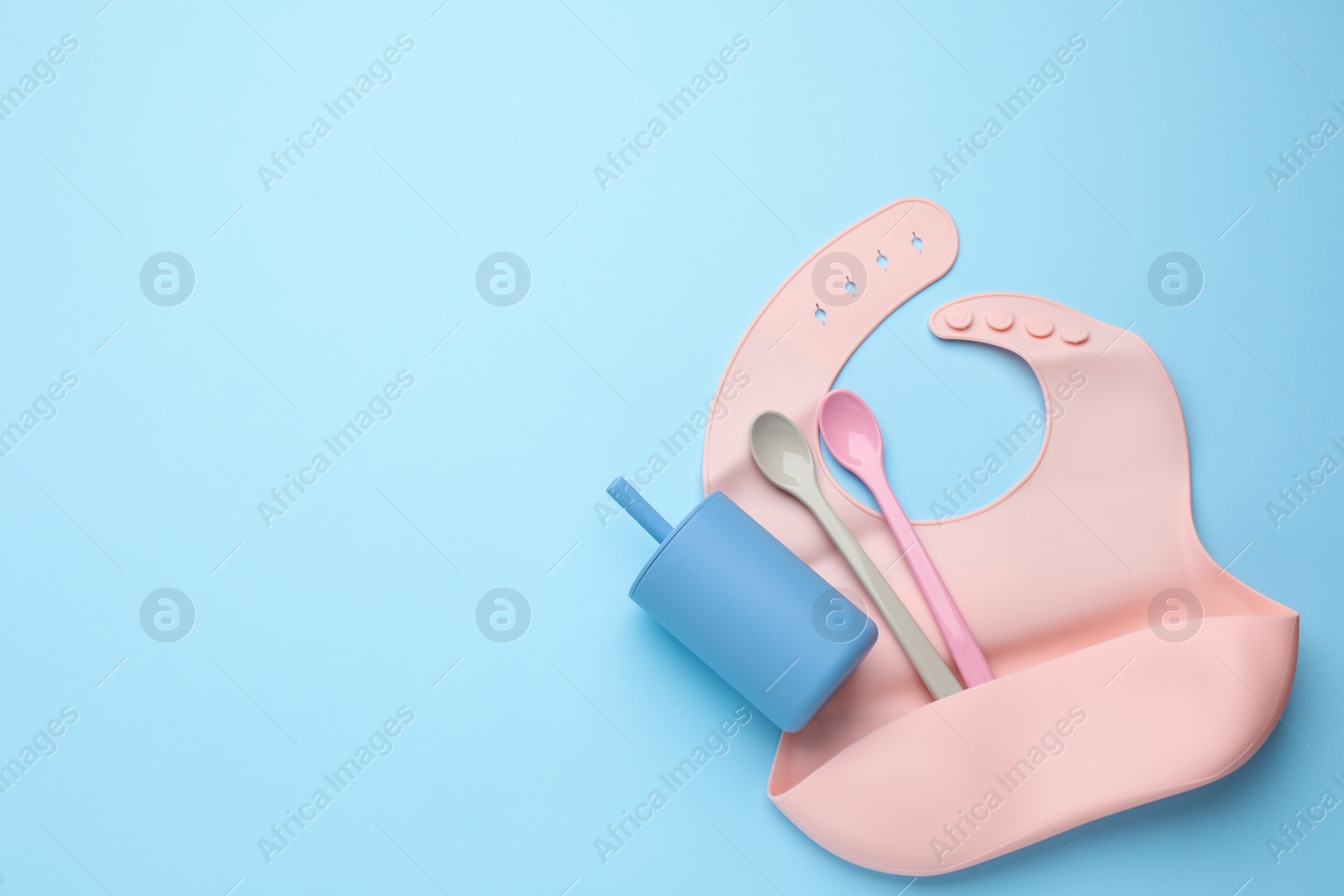 Photo of Baby feeding accessories and bib on light blue background, flat lay. Space for text