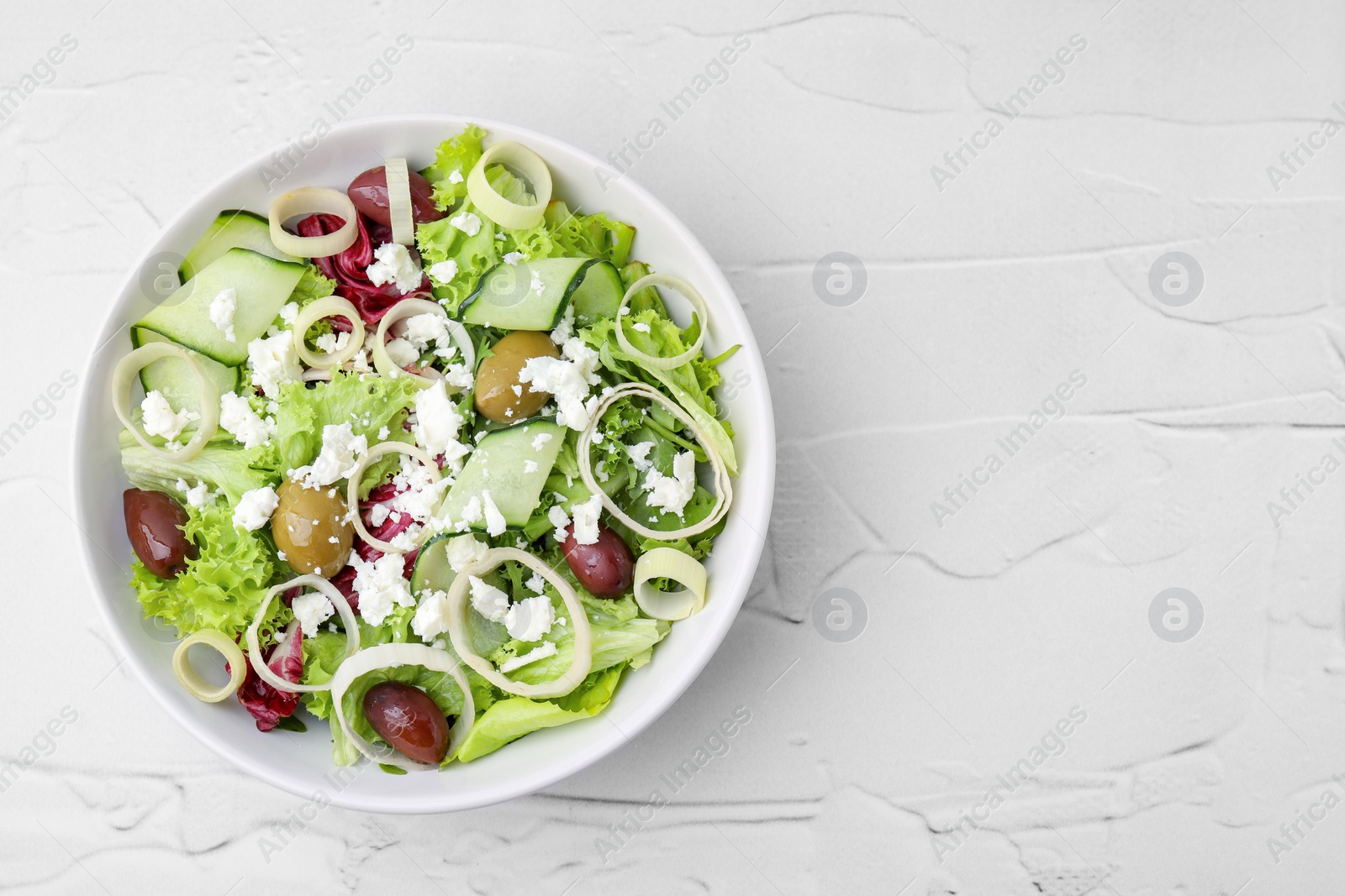 Photo of Bowl of tasty salad with leek, olives and cheese on white textured table, top view. Space for text