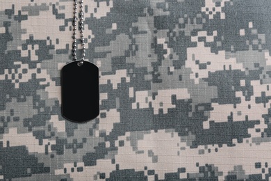 Photo of Military ID tag on camouflage background, top view. Space for text