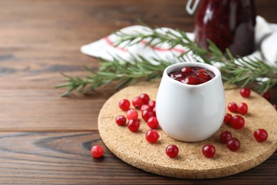 Photo of Cranberry sauce in pitcher fresh berries and rosemary on wooden table, closeup. Space for text