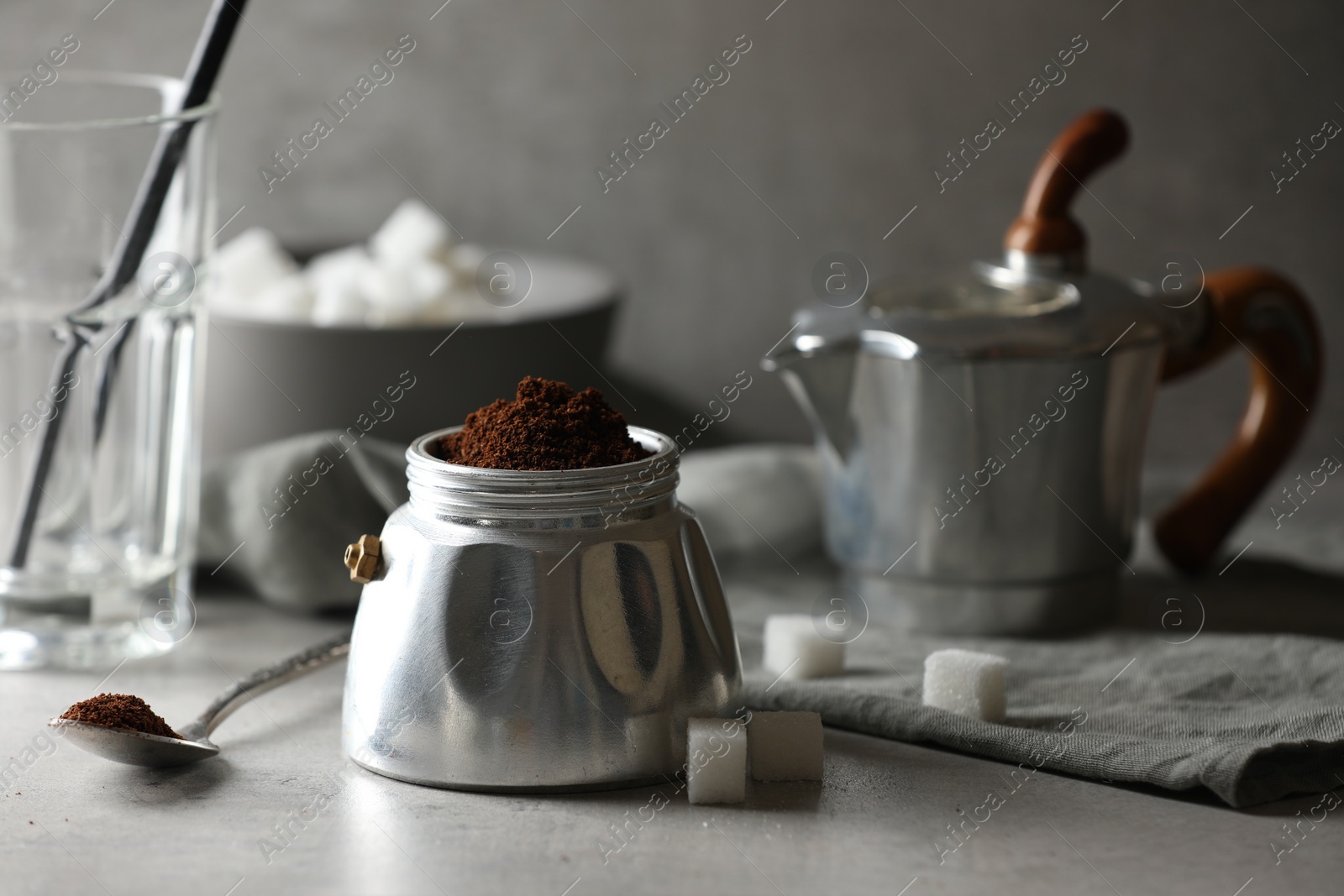 Photo of Ground coffee in moka pot and sugar cubes on light grey table, closeup