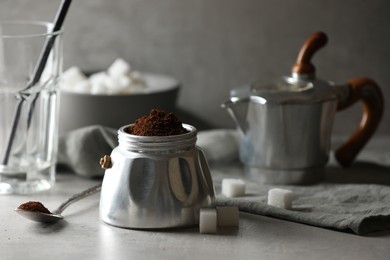 Ground coffee in moka pot and sugar cubes on light grey table, closeup