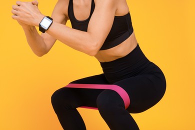 Photo of Woman exercising with elastic resistance band on orange background, closeup