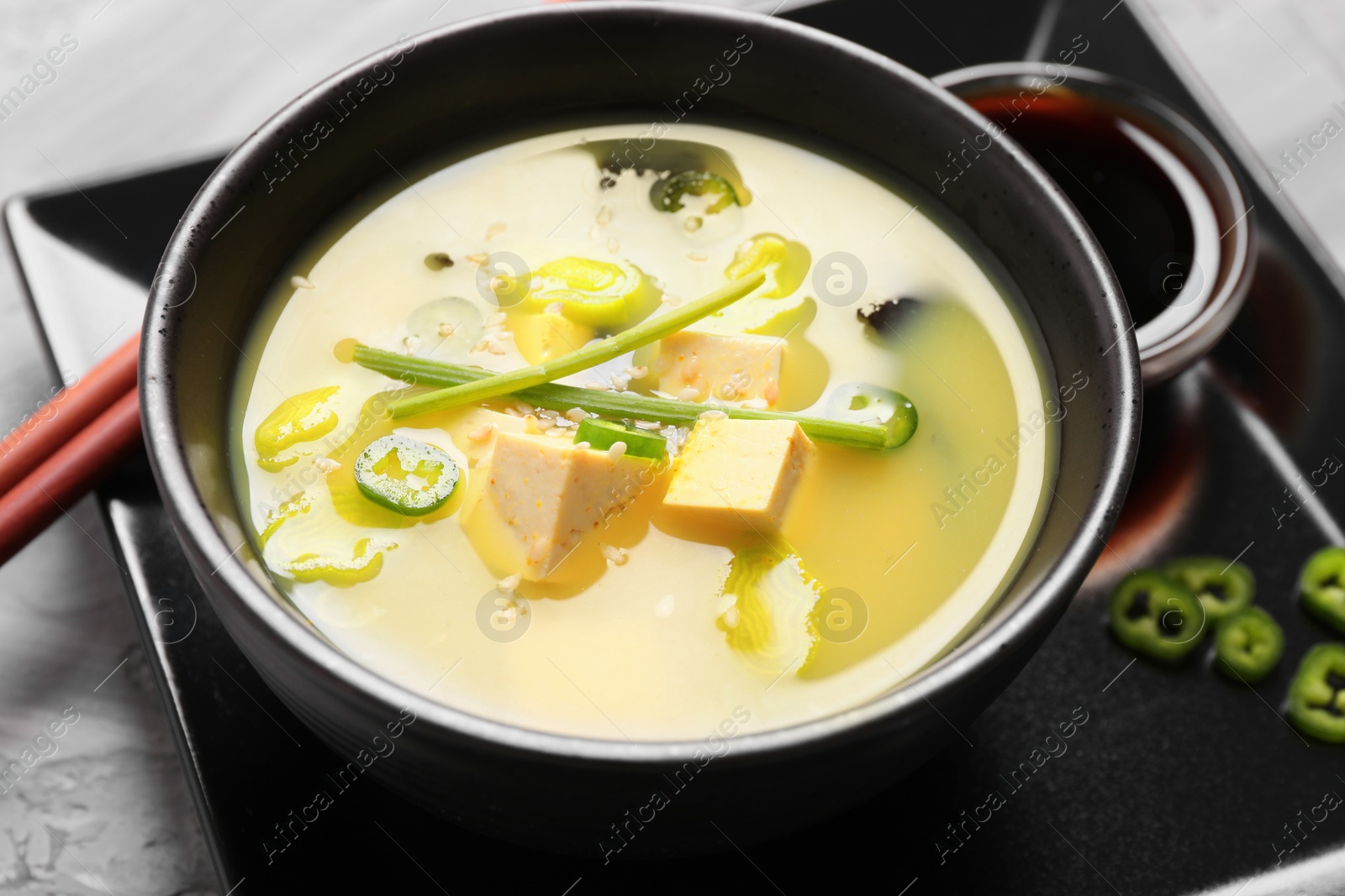 Photo of Bowl of delicious miso soup with tofu on table, closeup